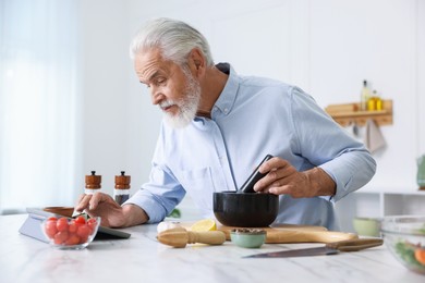 Photo of Elderly man using tablet while cooking at white marble table in kitchen