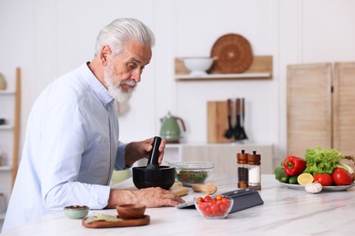 Photo of Elderly man using tablet while cooking at white marble table in kitchen