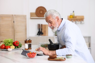 Photo of Elderly man using tablet while cooking at white marble table in kitchen