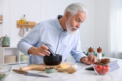 Photo of Elderly man using tablet while cooking at white marble table in kitchen