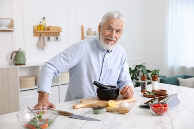 Photo of Elderly man cooking at white marble table in kitchen