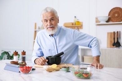 Photo of Elderly man cooking at white marble table in kitchen