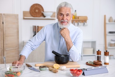 Photo of Elderly man cooking at white marble table in kitchen