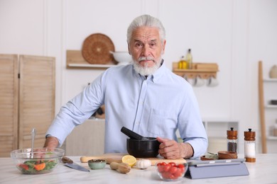 Photo of Elderly man cooking at white marble table in kitchen