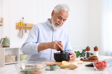 Photo of Elderly man cooking at white marble table in kitchen
