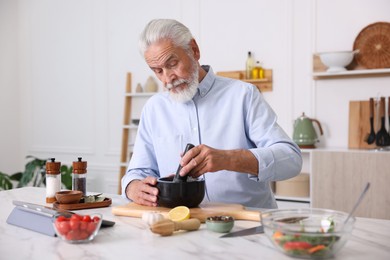 Photo of Elderly man cooking at white marble table in kitchen