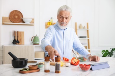 Photo of Elderly man cooking at white marble table in kitchen