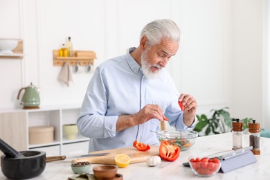 Photo of Elderly man cooking at white marble table in kitchen