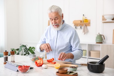 Photo of Elderly man cooking at white marble table in kitchen