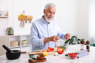 Photo of Elderly man cooking at white marble table in kitchen