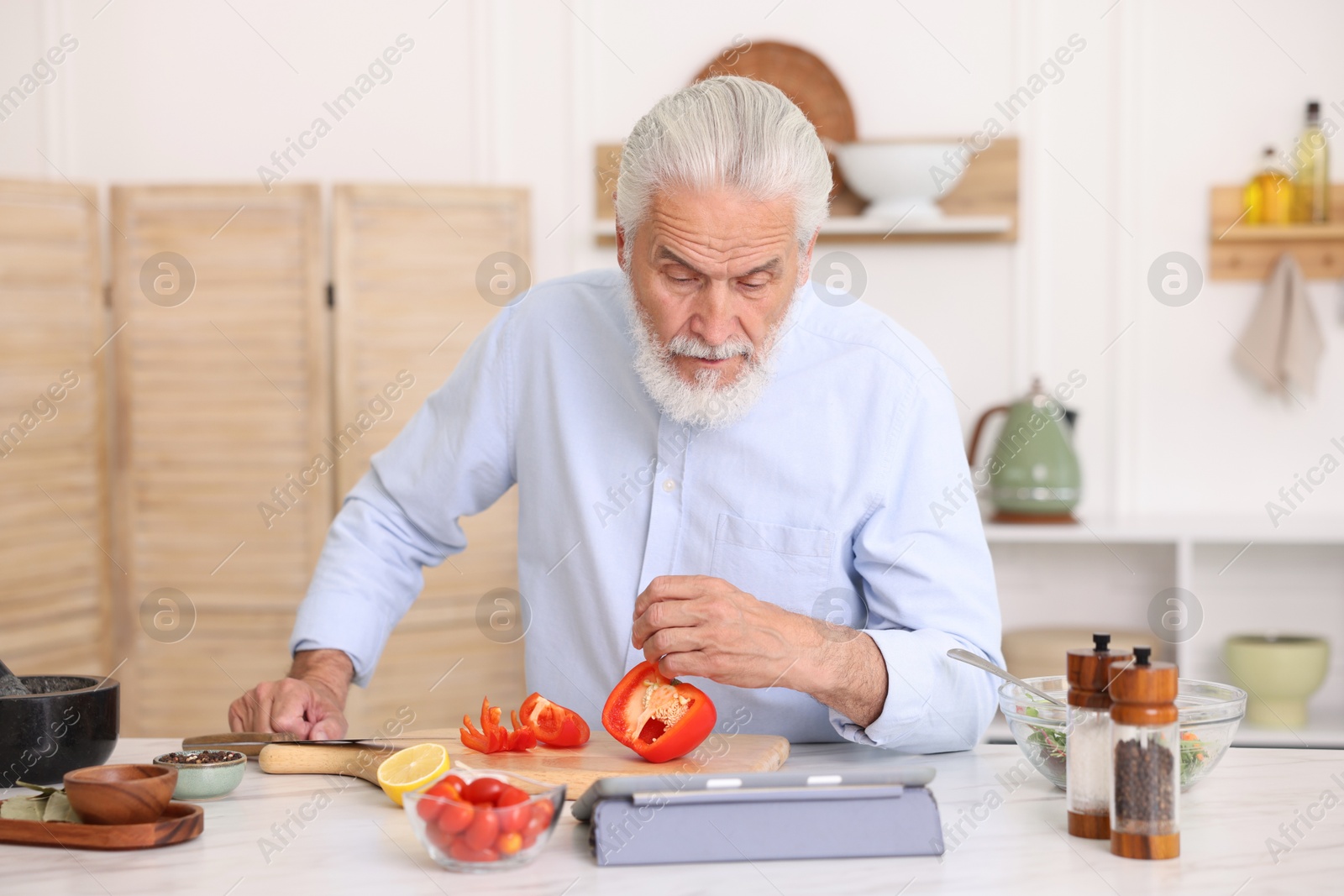 Elderly man using tablet while cooking at white marble table in kitchen Photo of Elderly man using tablet while cooking at white marble table in kitchen