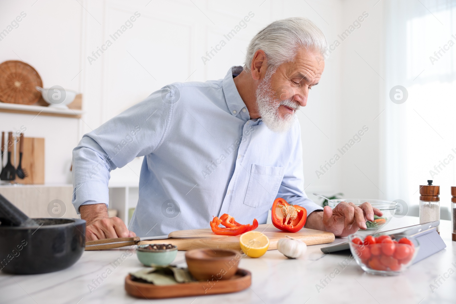 Elderly man using tablet while cooking at white marble table in kitchen Photo of Elderly man using tablet while cooking at white marble table in kitchen