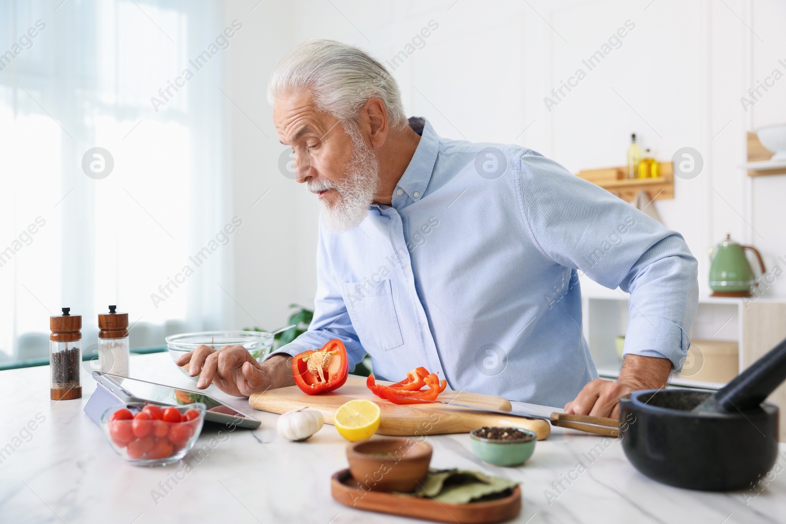 Elderly man using tablet while cooking at white marble table in kitchen Photo of Elderly man using tablet while cooking at white marble table in kitchen