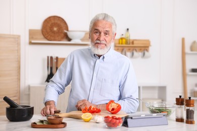 Photo of Elderly man cooking at white marble table in kitchen