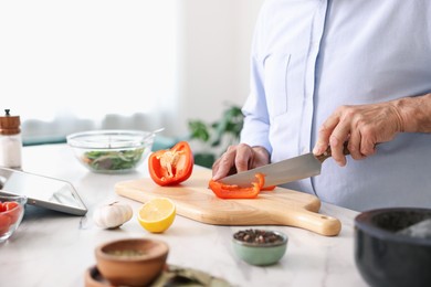 Photo of Elderly man cooking at white marble table in kitchen, closeup