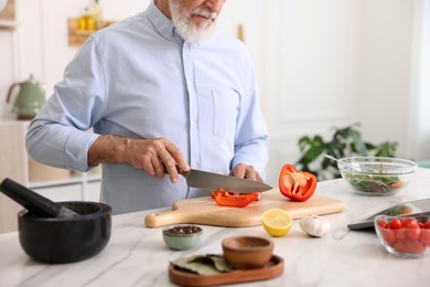 Photo of Elderly man cooking at white marble table in kitchen, closeup