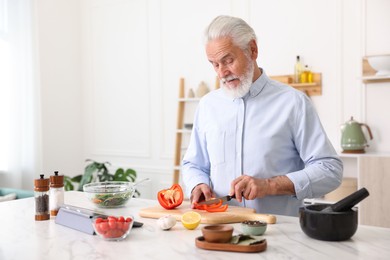 Photo of Elderly man cooking at white marble table in kitchen