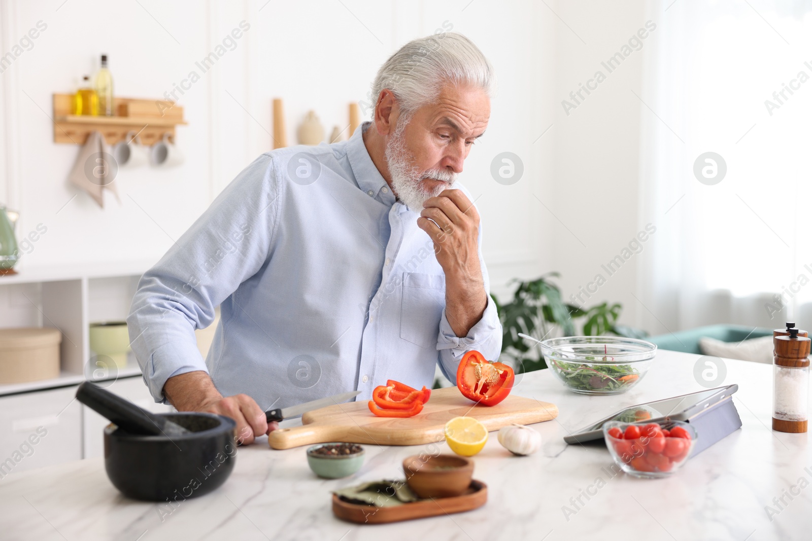 Elderly man using tablet while cooking at white marble table in kitchen Photo of Elderly man using tablet while cooking at white marble table in kitchen