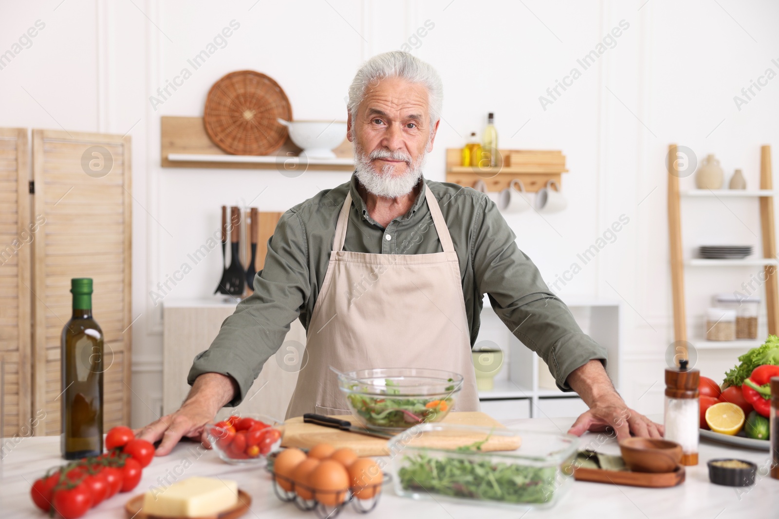 Elderly man cooking salad at white marble table in kitchen Photo of Elderly man cooking salad at white marble table in kitchen