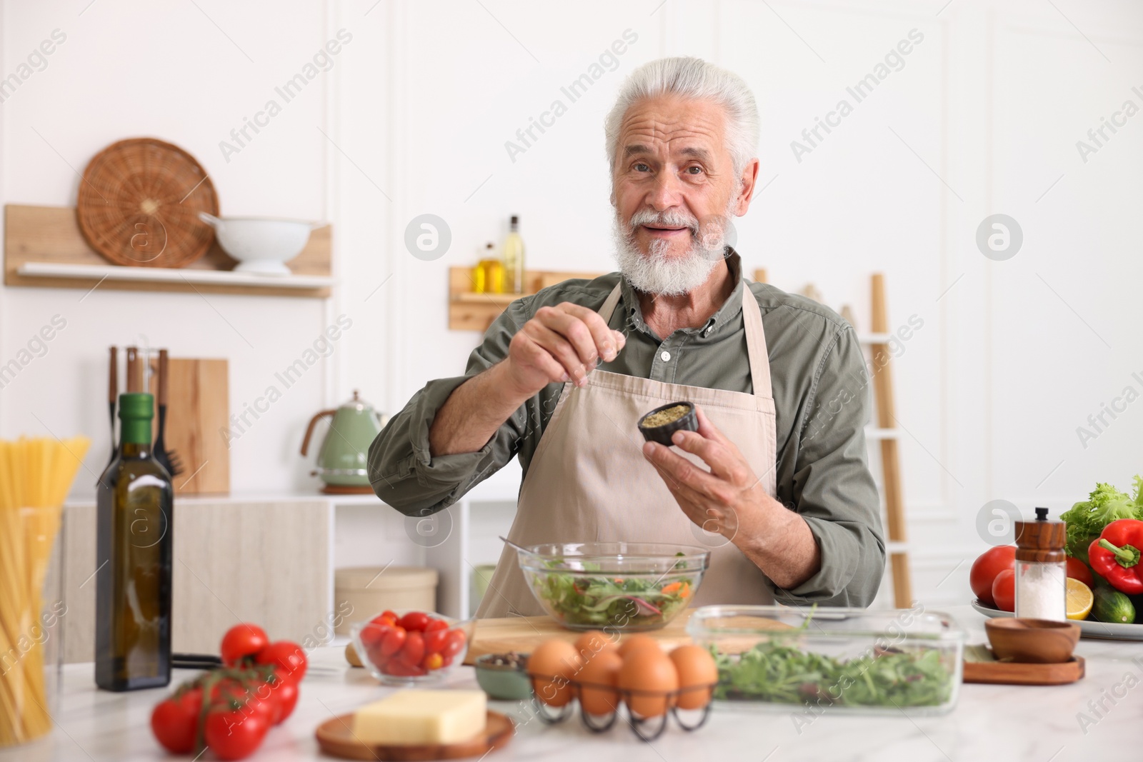 Elderly man cooking salad at white marble table in kitchen Photo of Elderly man cooking salad at white marble table in kitchen