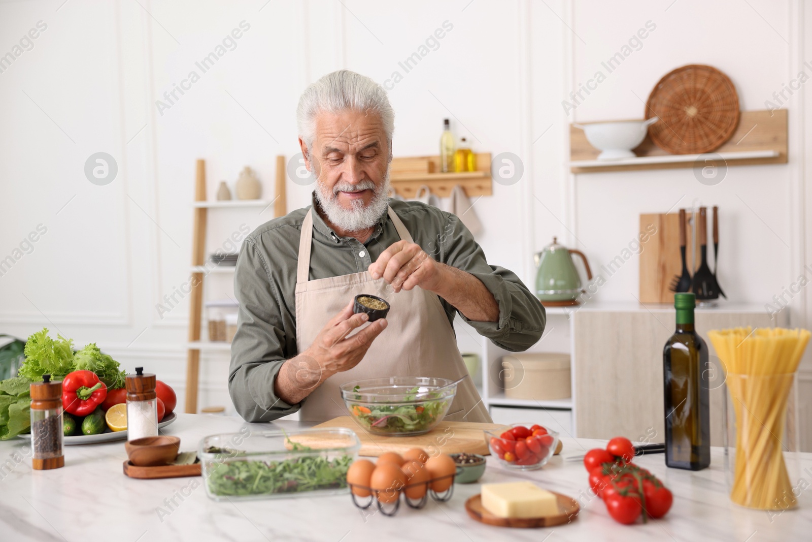 Elderly man cooking salad at white marble table in kitchen Photo of Elderly man cooking salad at white marble table in kitchen