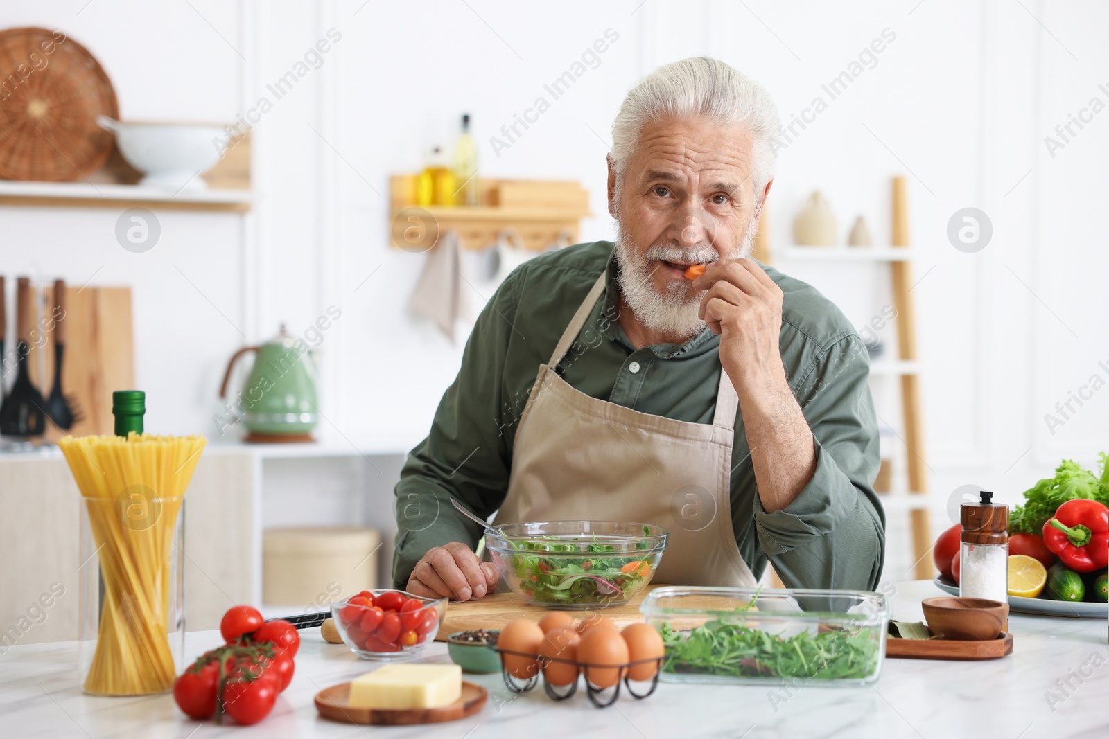 Elderly man cooking salad at white marble table in kitchen Photo of Elderly man cooking salad at white marble table in kitchen