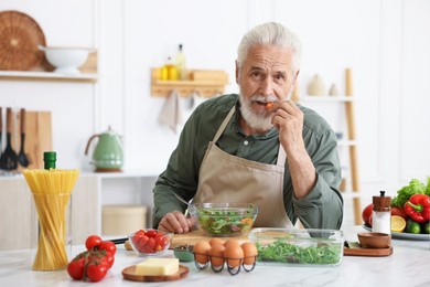 Photo of Elderly man cooking salad at white marble table in kitchen