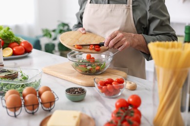 Photo of Elderly man cooking salad at white marble table in kitchen, closeup