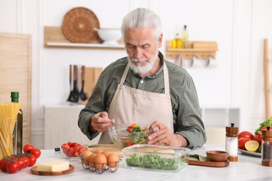 Photo of Elderly man cooking salad at white marble table in kitchen