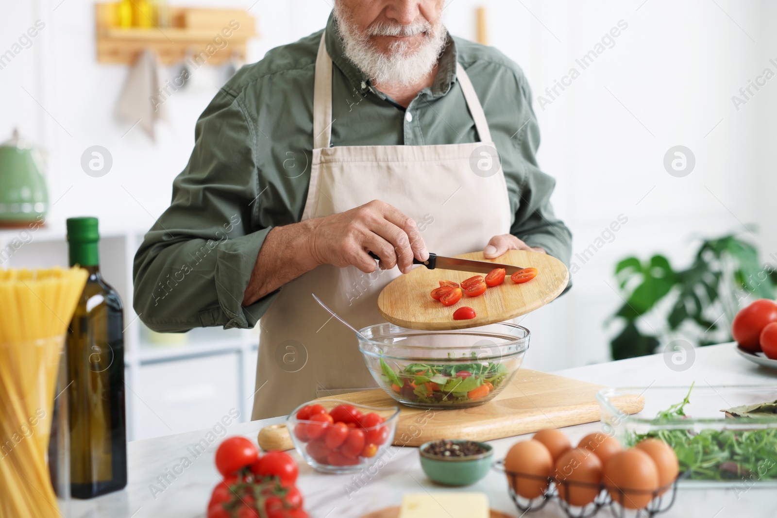 Elderly man cooking salad at white marble table in kitchen, closeup Photo of Elderly man cooking salad at white marble table in kitchen, closeup