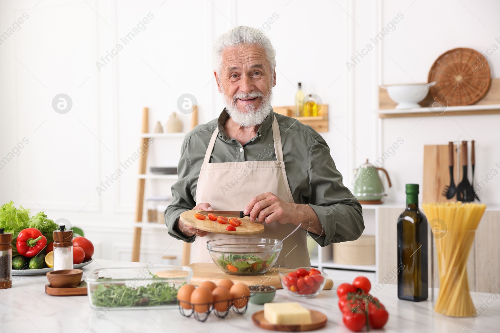 Elderly man cooking salad at white marble table in kitchen Photo of Elderly man cooking salad at white marble table in kitchen