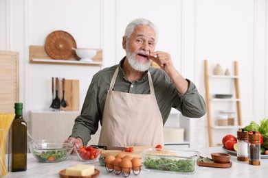 Photo of Elderly man cooking at white marble table in kitchen