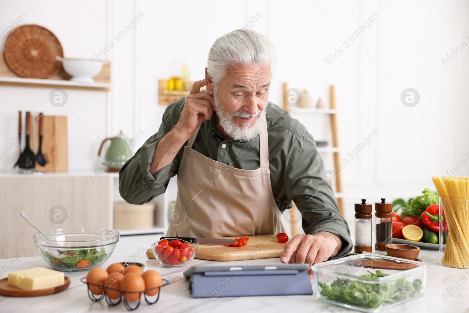 Elderly man using tablet while cooking at white marble table in kitchen Photo of Elderly man using tablet while cooking at white marble table in kitchen