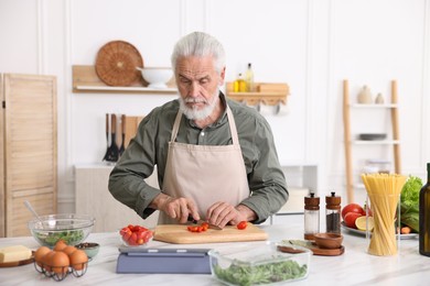Photo of Elderly man cooking at white marble table in kitchen