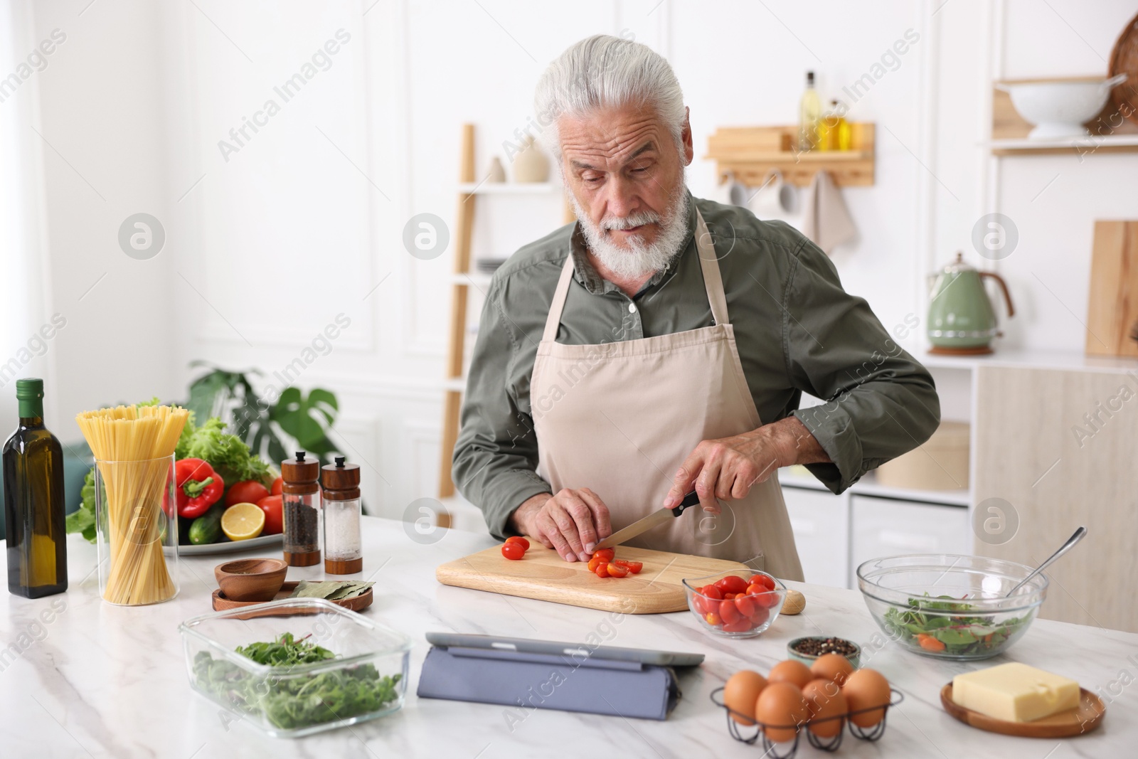 Elderly man cooking at white marble table in kitchen Photo of Elderly man cooking at white marble table in kitchen