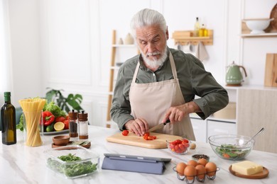 Photo of Elderly man cooking at white marble table in kitchen