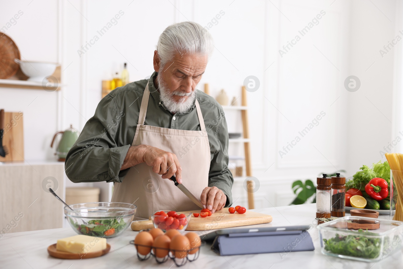 Elderly man cooking at white marble table in kitchen Photo of Elderly man cooking at white marble table in kitchen
