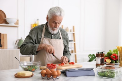 Photo of Elderly man cooking at white marble table in kitchen