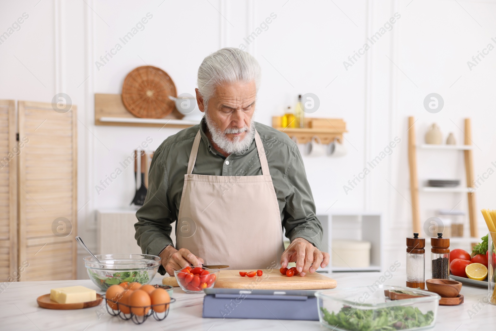 Elderly man cooking at white marble table in kitchen Photo of Elderly man cooking at white marble table in kitchen