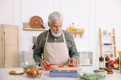 Photo of Elderly man cooking at white marble table in kitchen