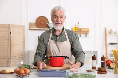 Photo of Elderly man cooking at white marble table in kitchen