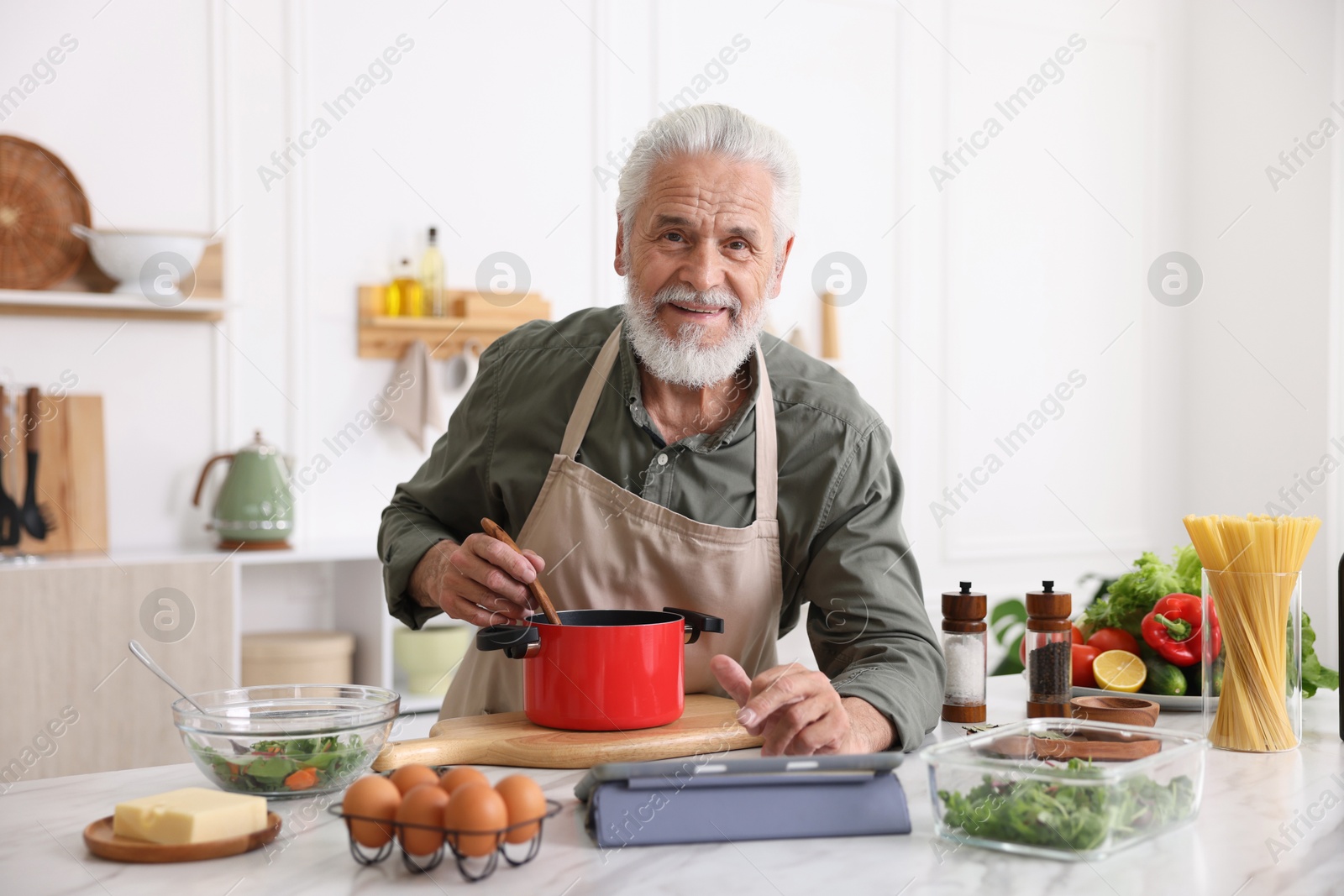 Elderly man using tablet while cooking at white marble table in kitchen Photo of Elderly man using tablet while cooking at white marble table in kitchen