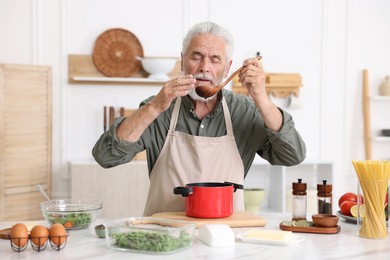 Photo of Elderly man cooking at white marble table in kitchen