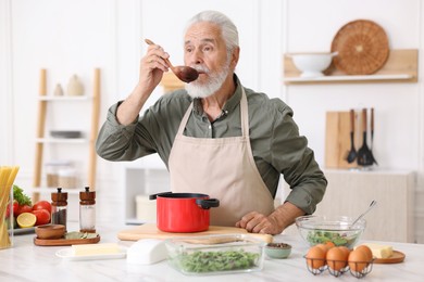 Photo of Elderly man cooking at white marble table in kitchen