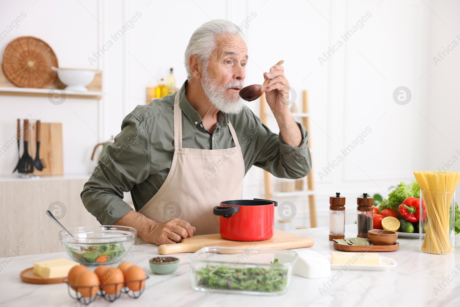 Elderly man cooking at white marble table in kitchen Photo of Elderly man cooking at white marble table in kitchen