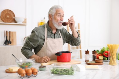 Photo of Elderly man cooking at white marble table in kitchen