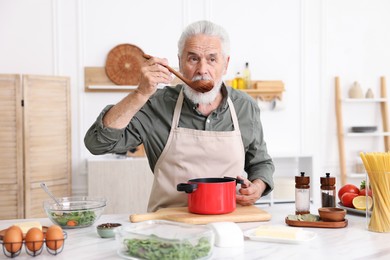 Photo of Elderly man cooking at white marble table in kitchen