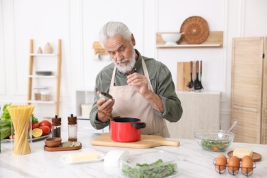 Photo of Elderly man cooking at white marble table in kitchen