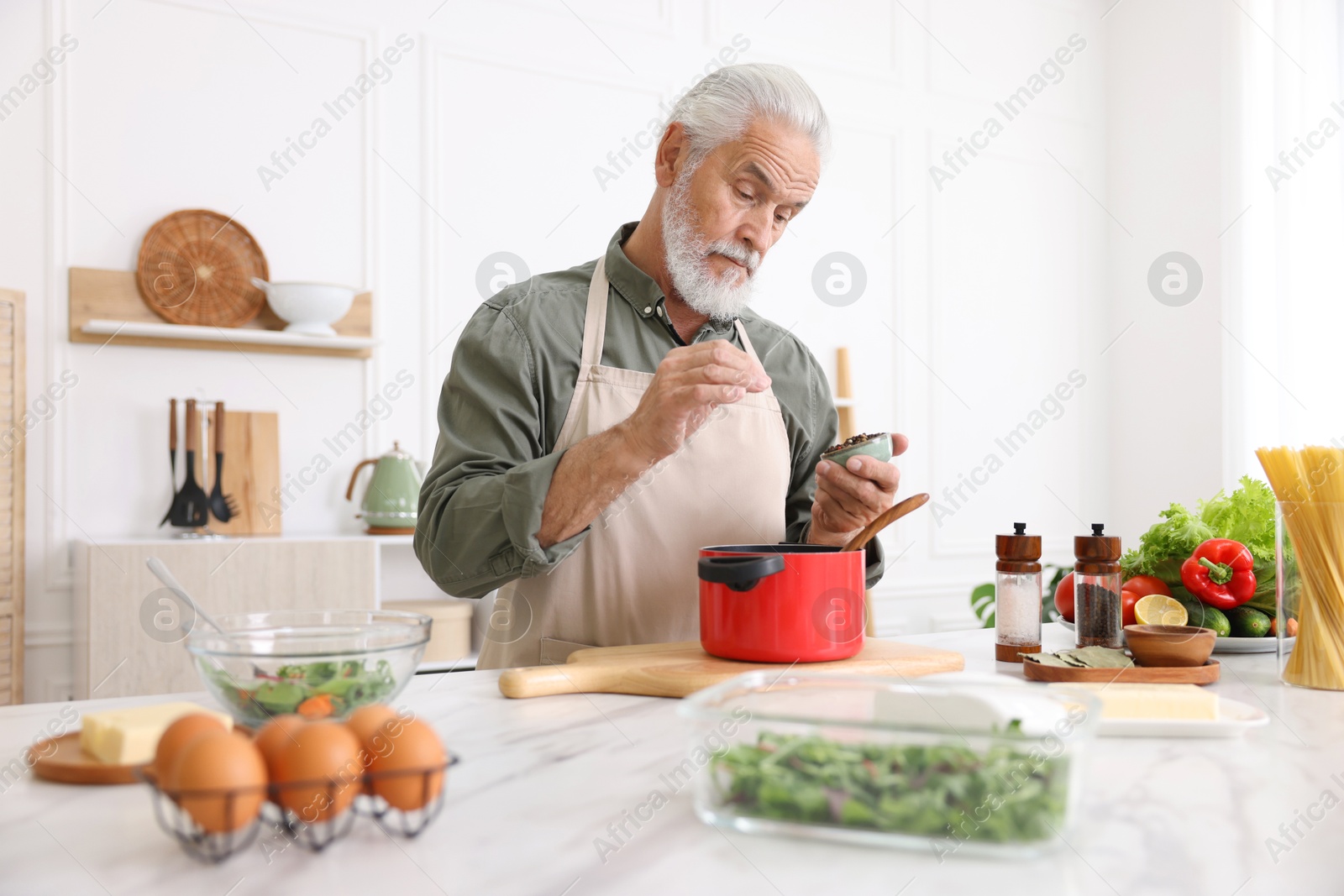 Elderly man cooking at white marble table in kitchen Photo of Elderly man cooking at white marble table in kitchen