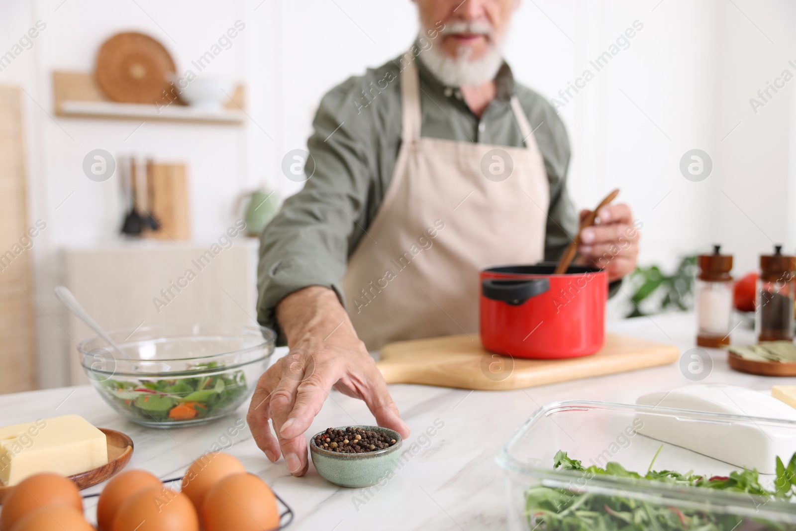 Elderly man cooking at white marble table in kitchen, closeup Photo of Elderly man cooking at white marble table in kitchen, closeup